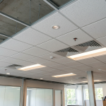 Obraz przedstawia wnętrze nowoczesnego biura w trakcie prac wykończeniowych lub częściowej aranżacji, skupiając się na systemowym suficie kasetonowym